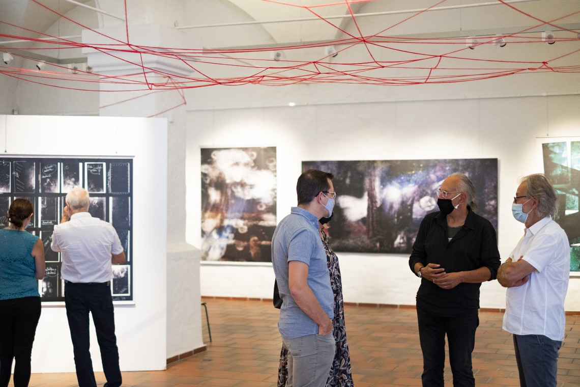 Blick in die Ausstellung: Menschen mit Schutzmasken betrachten Bilder, unterhalten sich