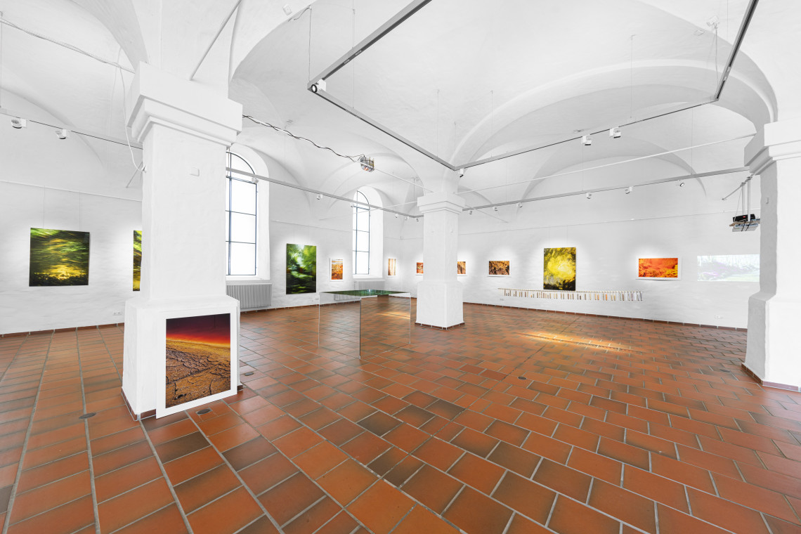 Blick in den Ausstellungsraum European Rivers (mit Fotoaufnahmen an den Wänden, Glaskasten in der Mitte des Raums und in einer Linie hängenden Reagenzgläsern 