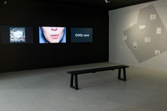 Schwarze Wand mit Video. Es zeigt den Mundbereich einer Frau vor blauem Hintergrund.